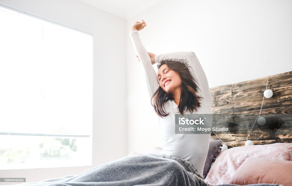 Cropped shot of a young woman stretching while sitting in her bed